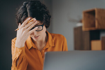 Frustrated tired young Spanish woman office worker in glasses covering face with hand