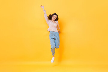 Cheerful Asian woman in casual clothes smiling and jumping with hand up in colorful yellow color...