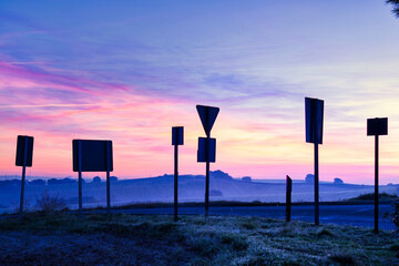 Silhouettes of numerous traffic signs backlit by dawn.