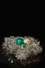 White and green Christmas baubles nested in a silver Christmas tinsel on a black background