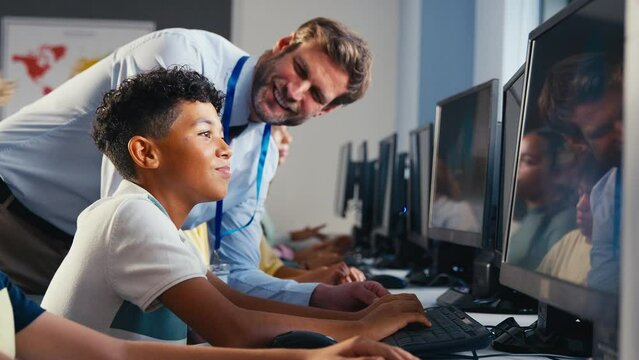 Male teacher helping multi-cultural group of secondary or high school students at computers in IT class with male teacher - shot in slow motion