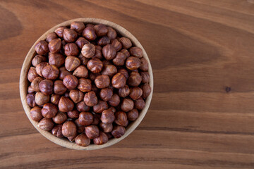 Top view of a bowl full of peeled hazelnuts on wooden table
