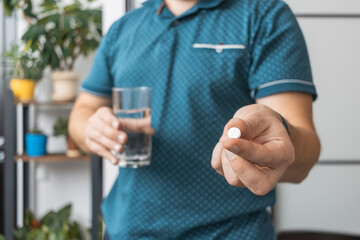Man taking medicine, holding in a hand white therapeutic pill, antibiotics, painkiller and glass of water, close-up view