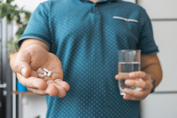 Man taking medicine, holding in a hand various therapeutic pills, antibiotics, painkiller and glass of water, close-up view