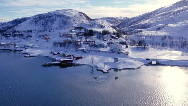 Snow covered mountain range on coastline in winter, Norway. Surroundings of town Tromso. Panoramic aerial view landscape of nordic snow cowered mountains, houses and ocean. Troms county, Fjordgard