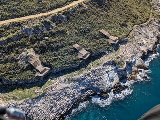 Aerial view of massive reinforced concrete artillery bunkers along the Albanian coast, built during the Hoxha era, showing Cold War military defense structures integrated into the coastal landscape.