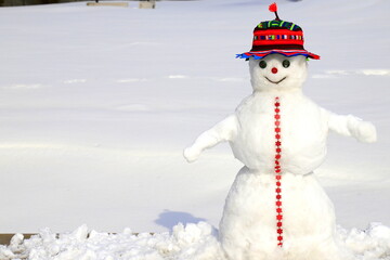 Obraz premium A funny snowman in red hat stands on snow covered meadow in winter, Christmas, New Year holidays, children entertainment and sports