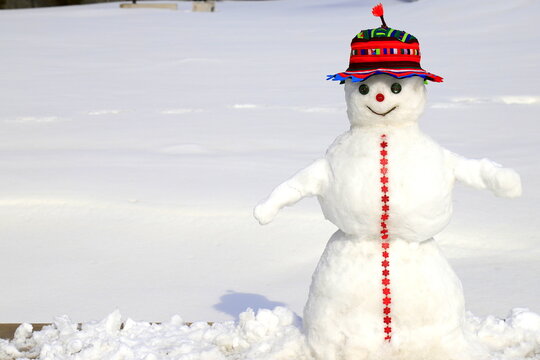 A funny snowman in red hat stands on snow covered meadow in winter, Christmas, New Year holidays, children entertainment and sports