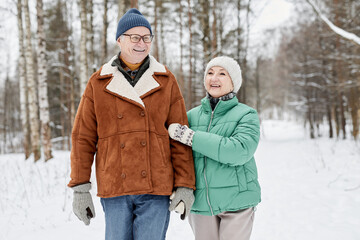 Happy senior husband and wife walking in winter park on cold
