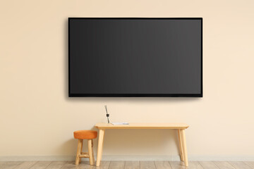 Modern smart TV set hanging on beige wall in room