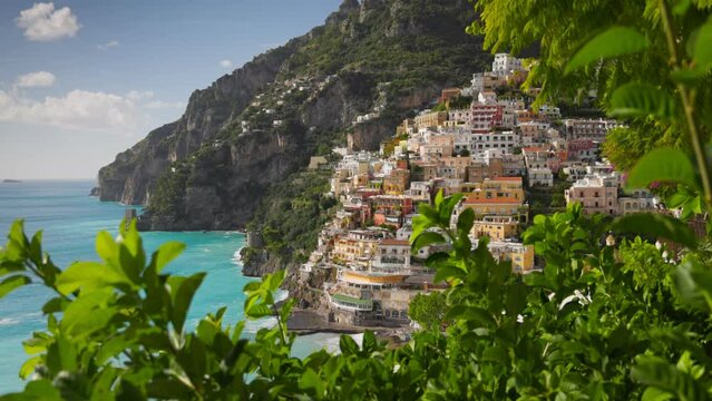 Beautiful Positano village, Amalfi coast, Italy. Camera moves between green leaves, overlooking the beach with turquoise water, colorful houses and mountains in Positano village. Steadycam shot, 4K