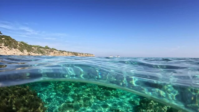 Camera slowly move into clear turquoise sea water on the coast of Cyprus. Split slow motion shot of crystal clear water in blue lagoon beach, Cyprus. Famous summer destination, half underwater