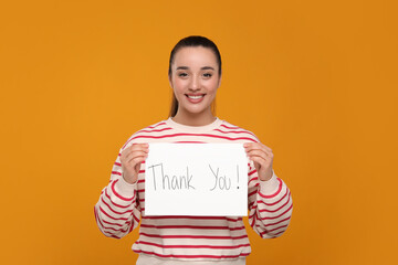 Happy woman holding card with phrase Thank You on orange background