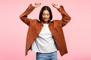 Smiling Asian woman wearing casual brown shirt holding hands up isolated on pink background