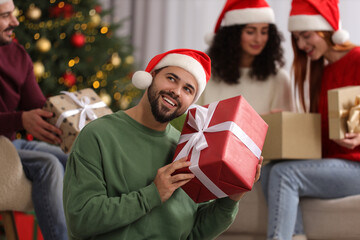 Christmas celebration in circle of friends. Happy young man with gift box at home, selective focus