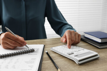 Woman using calculator while taking notes at wooden table, closeup