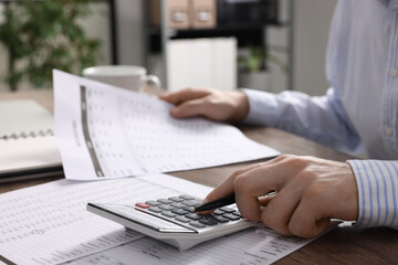 Naklejka premium Man working with data using calculator at wooden table indoors, closeup