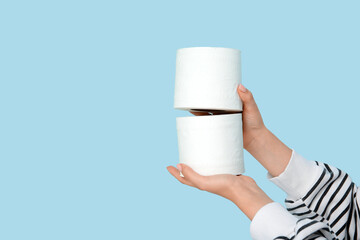 Female hands with toilet paper rolls against color wall, closeup