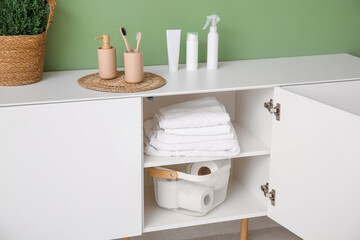 Chest of drawers with toilet paper rolls, clean towels and bath supplies in restroom, closeup