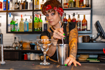 Cute young bartender preparing a cocktail and looking at camera