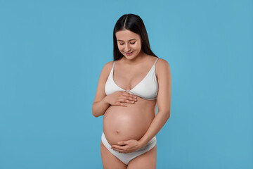Beautiful pregnant woman in stylish comfortable underwear on light blue background