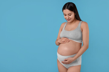 Beautiful pregnant woman in comfortable maternity underwear on light blue background, space for text
