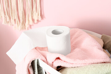 Basket with laundry and toilet paper roll near color wall, closeup