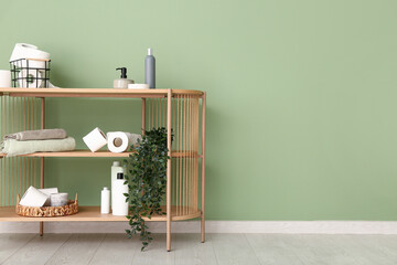 Wooden rack with toilet paper rolls, bath supplies and plant near color wall