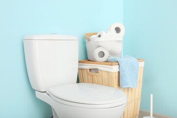 Toilet bowl and laundry basket with paper rolls near color wall