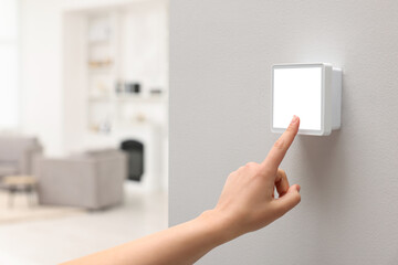Woman adjusting thermostat on white wall indoors, closeup and space for text. Smart home system