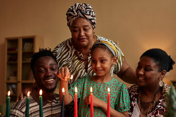 Cheerful family lightning candles in holder prepared for Kwanzaa celebration