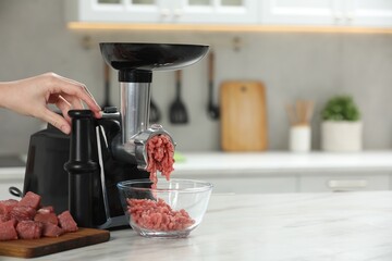 Woman making beef mince with electric meat grinder at white table in kitchen, closeup. Space for text
