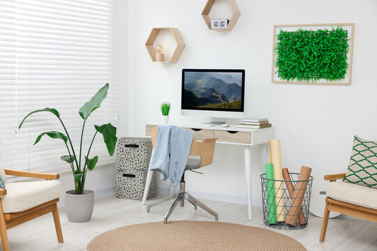 Green artificial plant wall panel and desk with computer in light room. Interior design