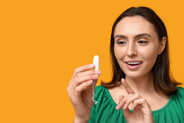 Beautiful young woman with tampon on yellow background