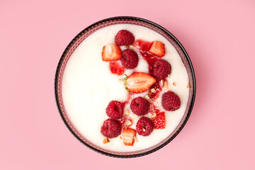 Bowl of tasty semolina porridge with fresh berries on pink background