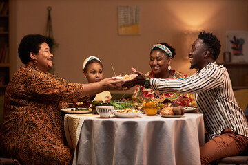 Smiling woman giving bowl of salad to her son-in-law to family dinner