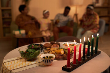 Colorful burning candles and tasty dishes on table in living room of family celebrating Kwanzaa