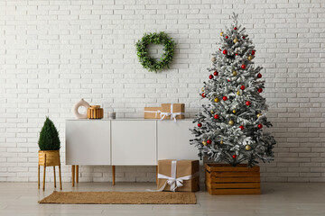 Beautiful Christmas tree with dresser and gift boxes near white brick wall