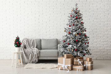Beautiful Christmas tree with sofa and gift boxes near white brick wall