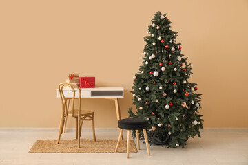 Beautiful Christmas tree with gift boxes and desk near beige wall