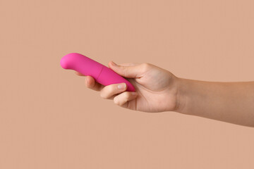 Female hand with pink vibrator on color background, closeup