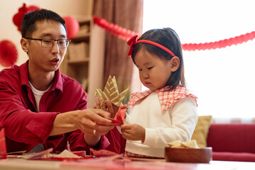 Portrait of cute Asian baby girl playing with paper cranes and red decorations for Chinese New Year...