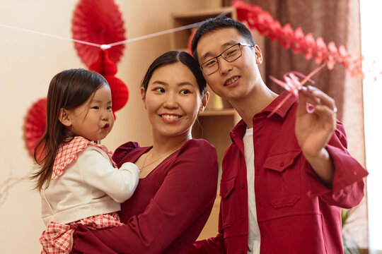 Waist up portrait of happy Asian family with baby girl decorating home for Chinese New Year together, all wearing red