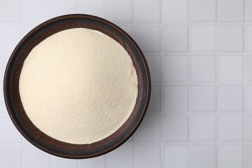 Uncooked organic semolina in bowl on white tiled table, top view. Space for text