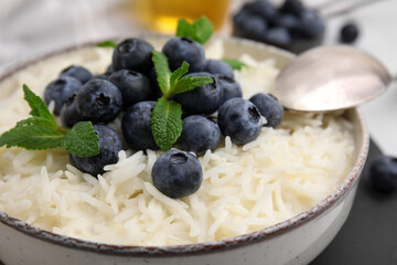 Bowl of delicious rice porridge with blueberries and mint on table, closeup
