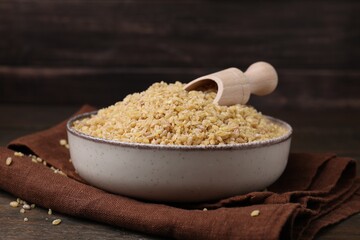 Bowl and scoop with raw bulgur on table, closeup