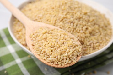 Bowl and spoon with raw bulgur on table, closeup