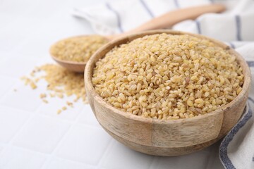 Raw bulgur in bowl on white table, closeup