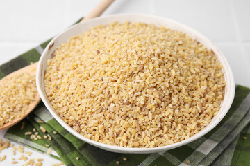 Raw bulgur in bowl on table, closeup