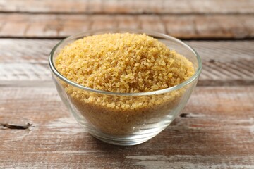 Raw bulgur in bowl on wooden table, closeup